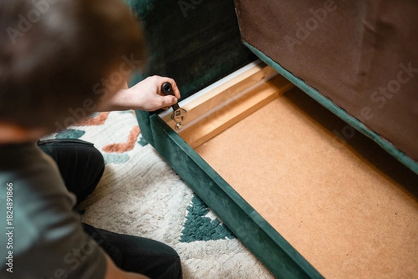 Fototapeta Man disassembling sofa furniture mechanism at home using furniture wrench. DIY Assembling Furniture concept.