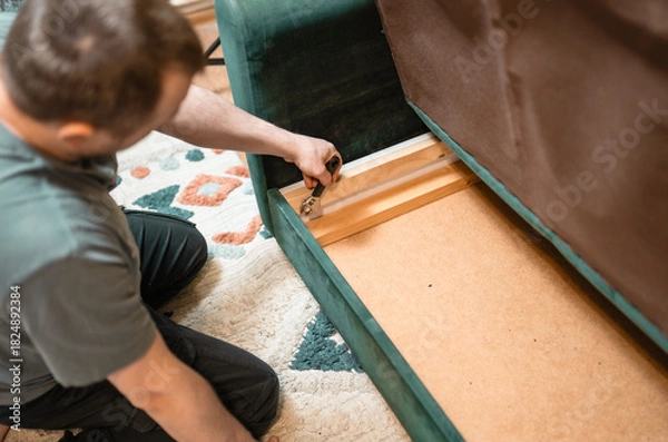 Fototapeta Man disassembling sofa furniture mechanism at home using furniture wrench. DIY Assembling Furniture concept.