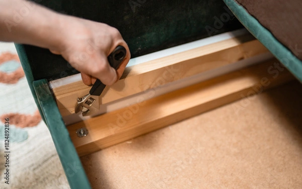 Fototapeta Man disassembling sofa furniture mechanism at home using furniture wrench. DIY Assembling Furniture concept.