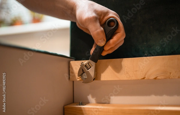 Fototapeta Man disassembling sofa furniture mechanism at home using furniture wrench. DIY Assembling Furniture concept.