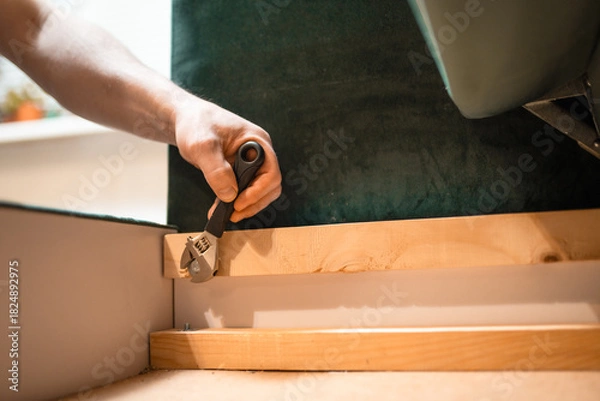 Fototapeta Man disassembling sofa furniture mechanism at home using furniture wrench. DIY Assembling Furniture concept.