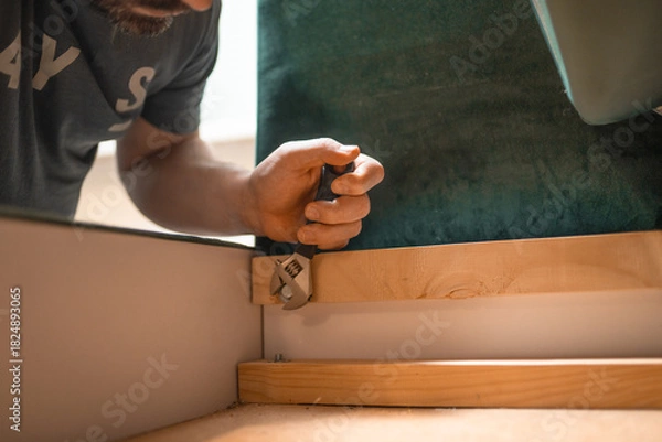 Fototapeta Man disassembling sofa furniture mechanism at home using furniture wrench. DIY Assembling Furniture concept.