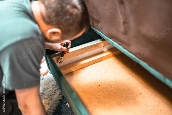 Fototapeta Man disassembling sofa furniture mechanism at home using furniture wrench. DIY Assembling Furniture concept.