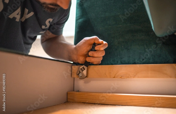Fototapeta Man disassembling sofa furniture mechanism at home using furniture wrench. DIY Assembling Furniture concept.
