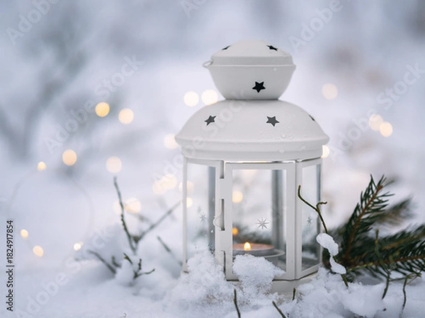 Fototapeta candle lantern stands in the snow in a forest. Christmas background with garland lights and copy space.
