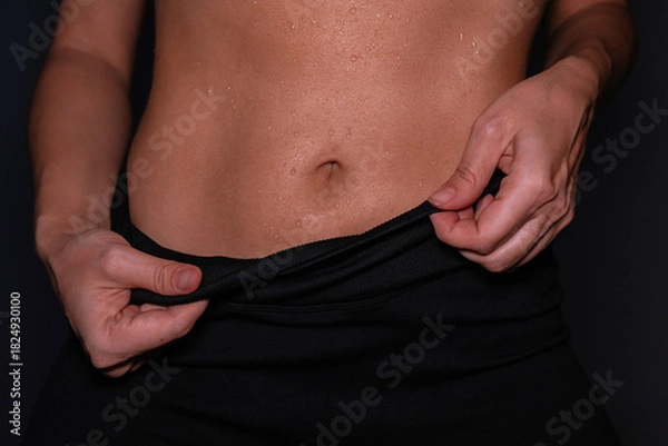 Fototapeta Young woman’s toned abdomen with visible sweat after workout on a dark background. Close-up of firm core and wet skin, highlighting fitness routine, body strength and active lifestyle. Female abs