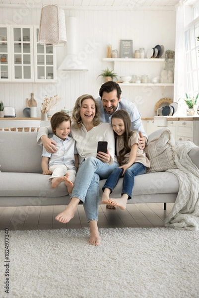 Obraz Happy mom dad two kids cuddle on couch using phone