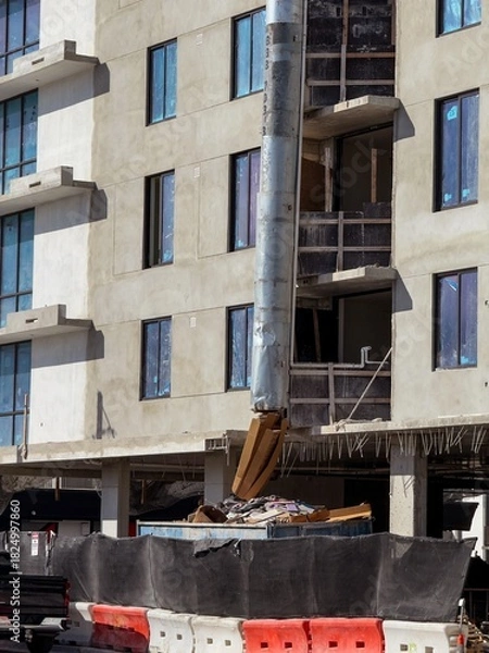 Fototapeta Suspended sections of metal garbage chute on a facade of building under construction 