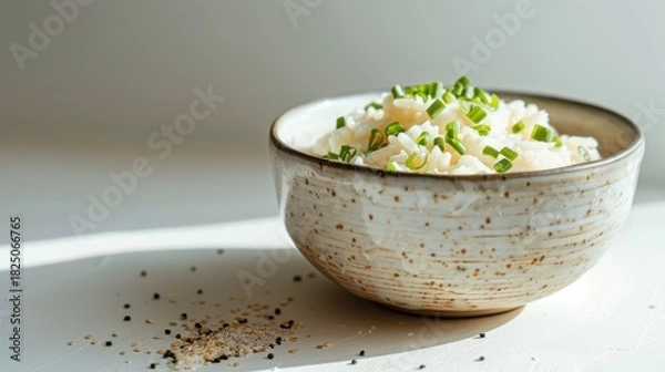Fototapeta A ceramic bowl of cooked white rice topped with freshly sliced green onions, set on a bright white surface with spices scattered below, emphasizing fresh, simple ingredients