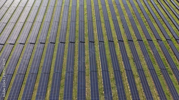 Obraz Aerial view of a large solar panel farm with rows of photovoltaic panels and green grass landscape