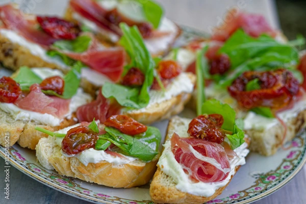 Obraz Bruschetta appetizer with prosciutto, ricotta, sun-dried tomatoes, arugula