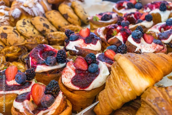 Fototapeta Assorted pastries with cream and fresh berries on the bakery counter. Close-up of sweet desserts. 
