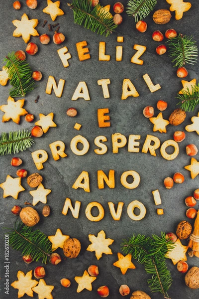 Fototapeta FELIZ NATAL COOKIES. Words Merry Christmas and Happy New Year en portuguese with baked cookies, Christmas decoration and nuts on black slate background. Christmas card for portuguese speaking