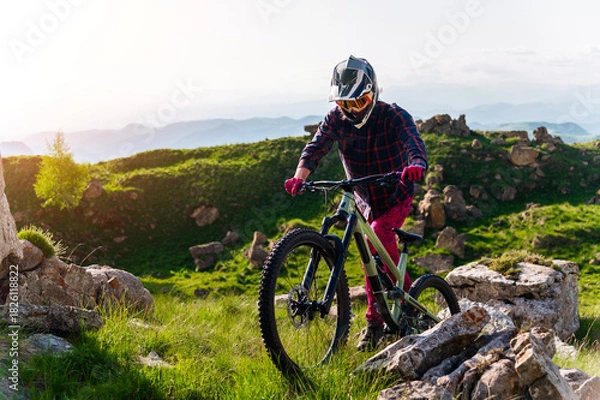 Obraz Cyclist in bright clothing climbs a rocky summer trail in clear weather. The concept is extreme sports and enduro, a challenging climb from bicycles up a mountain