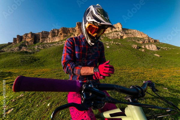 Obraz cyclist in special gear stands and adjusts his gloves. His gloved hands grip the handlebars. The athlete puts on clothing that will protect him in the event of a fall