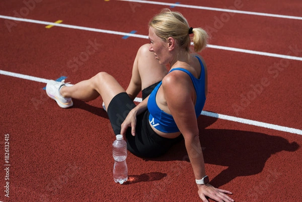 Fototapeta Tired happy runner resting after jogging sitting on treadmill and smiling. Young athletic runner resting after workout. Work harder, rest harder.