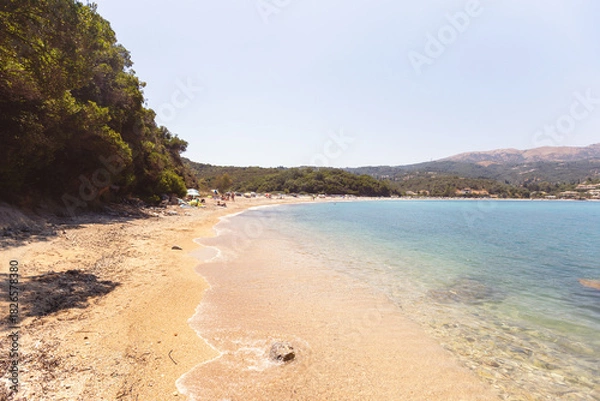 Obraz Idyllic sandy beach with turquoise water, gentle waves, and lush coastal greenery.