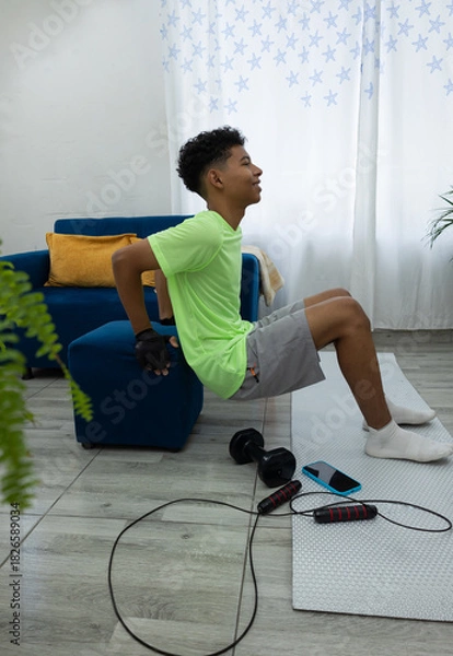 Obraz Young man doing tricep dips in his living room, with his hands on a pouf and his feet on a mat. Home workout routine focused on strength and well being