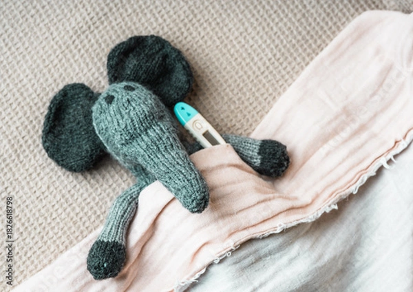 Fototapeta Toy elephant with thermometer lays covered with baby blanket- top view. Children Healthcare concept photo.