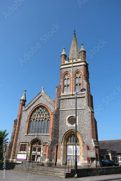 Fototapeta Methodist Church Building with Tall Steeple and Stained Glass Window Under Clear Blue Sky, Petersfield