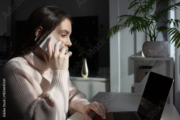 Obraz Woman talking on phone while working on laptop at home