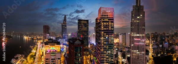 Obraz A city skyline at night with a large building in the middle. The city is lit up with lights and the sky is cloudy