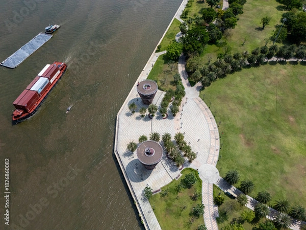 Obraz Boat is on the water near a park. The park has a walkway and a pond