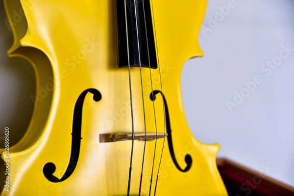 Obraz A yellow violin with a black bow. The violin is sitting on a wooden stand. The strings are visible and the bow is attached to the violin