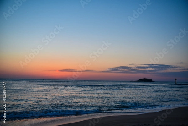 Obraz The ocean is calm and the sky is a beautiful shade of blue. The sun is setting and the sky is filled with a warm orange glow