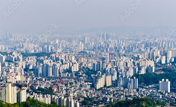 Obraz A city with many buildings and a large hill in the background. The sky is cloudy and the sun is not visible