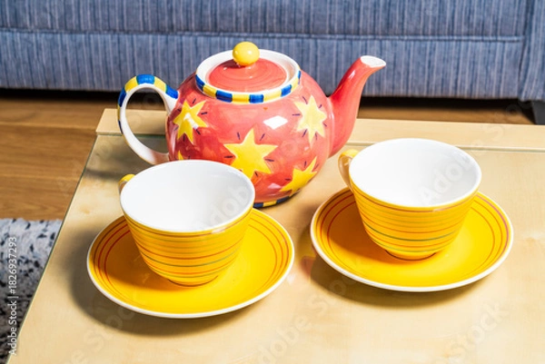 Fototapeta Two yellow cups and a bright colourful teapot in a living room setting, home comfort and relaxation concept