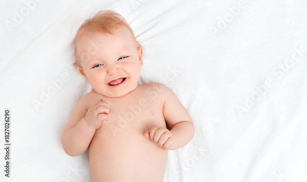 Fototapeta Happy ten-month-old baby lying on a white sheet with copy space