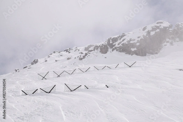 Obraz Snow-covered alpine rocks rise from a foggy winter slope, creating a dramatic and atmospheric mountain scene. Rugged terrain, soft light, and cold high-altitude conditions.