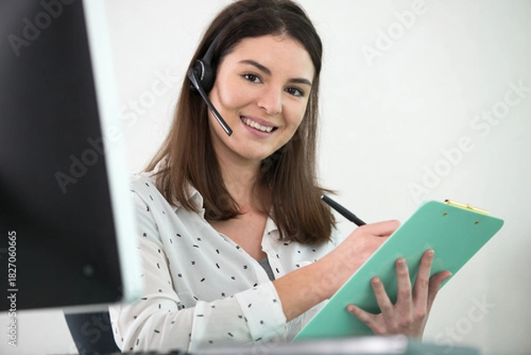 Obraz beautiful customer-servise operator with a headset taking notes