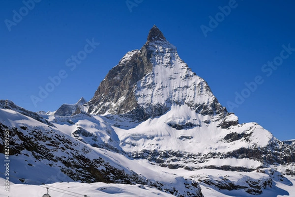 Fototapeta Close view of the Matterhorn covered in winter snow, rising sharply under a deep blue sky. Iconic Swiss alpine landscape with dramatic textures and prisitine mountain scenery.