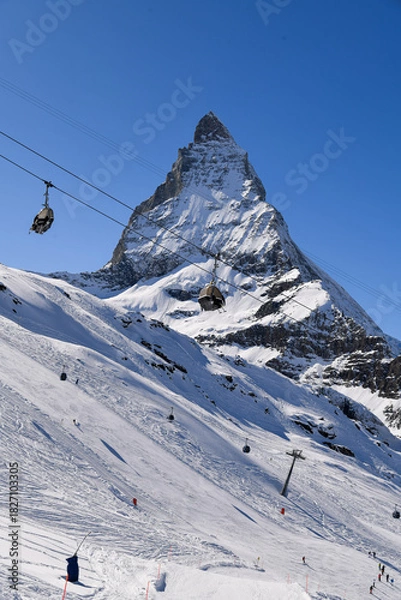 Fototapeta Ski lift gondolas passing above the snowy Matterhorn peak on a clear winter day. iconic swiss alpine scenery with dramatic mountain view and bright blue sky.