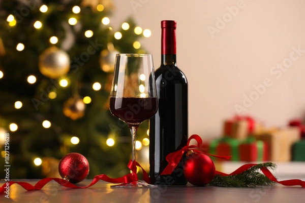 Obraz Glass of red wine, bottle and Christmas decor on wooden table against background with blurred lights