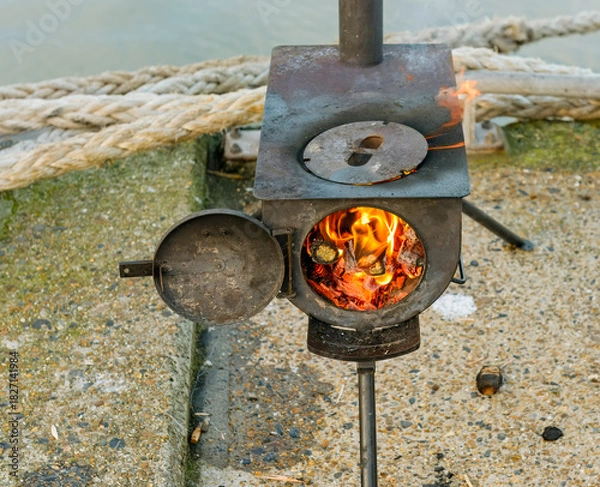 Obraz rusty metal portable wood stove with open round door showing the flames and burning wood
