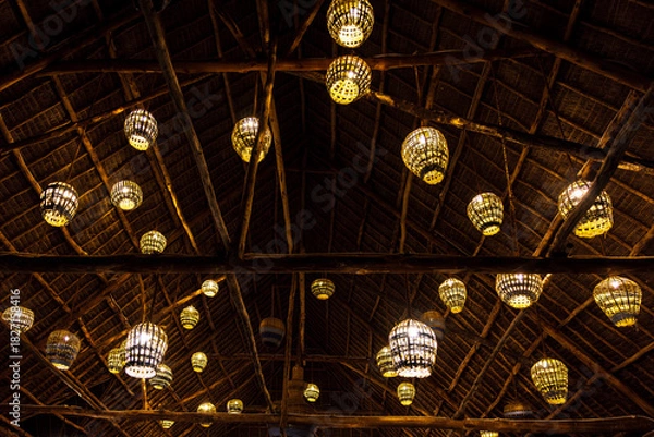 Obraz Rustic thatched roof illuminated by numerous glowing woven lanterns.
