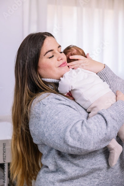 Fototapeta Mother gently hugging newborn baby with closed eyes