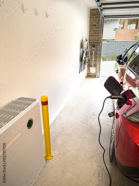 Obraz vertical shot Electric car EV plugged in on charge in a garage with active solar battery wall installation green light showing activity