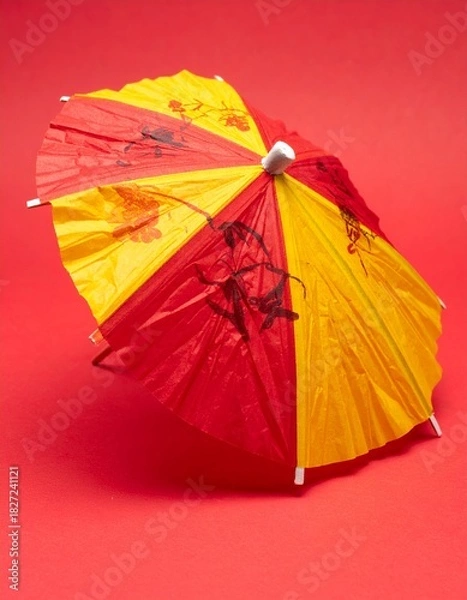 Fototapeta Vibrant Red and Yellow Cocktail Umbrella on a Striking Red Background, Perfect for Summer Drinks and Tropical Themes.