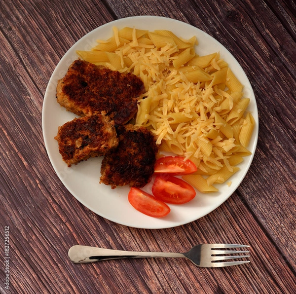 Obraz Fried meat cutlets, ripe tomato slices and macaroni sprinkled with cheese on a wooden table.