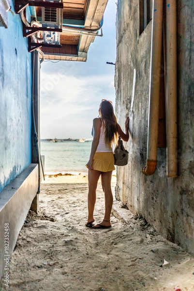 Fototapeta Woman exploring El Nido, Philippines, looking out to the ocean from a narrow alleyway