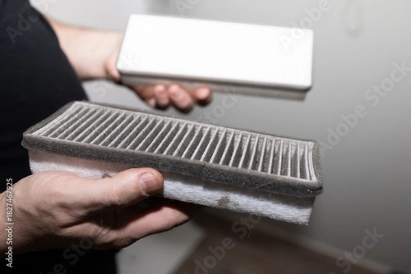 Obraz hands holding dirty cabin filter, homeowner inspecting used filter beside sealed replacement box in garage,
