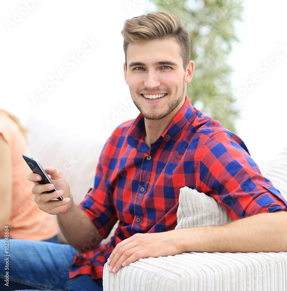 Fototapeta modern guy with a smartphone and his friends sitting on the couch