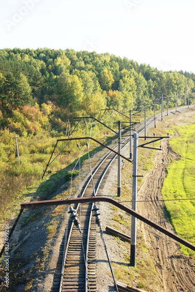 Fototapeta Siberian forest and empty railroad tracks with overhead catenary system stretching into distance. Symbolizes remote transportation routes, regional connectivity and sustainable mobility infrastructure