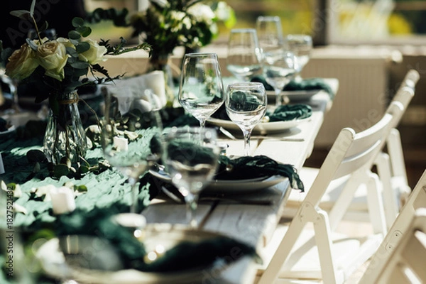 Fototapeta Elegant festive table setting with green decor and glassware