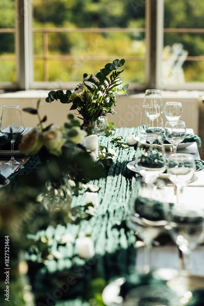 Fototapeta Elegant festive table setting with green decor and glassware