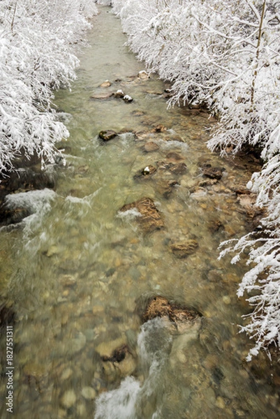 Fototapeta Fast flowing mountain stream framed by snow covered riverbanks